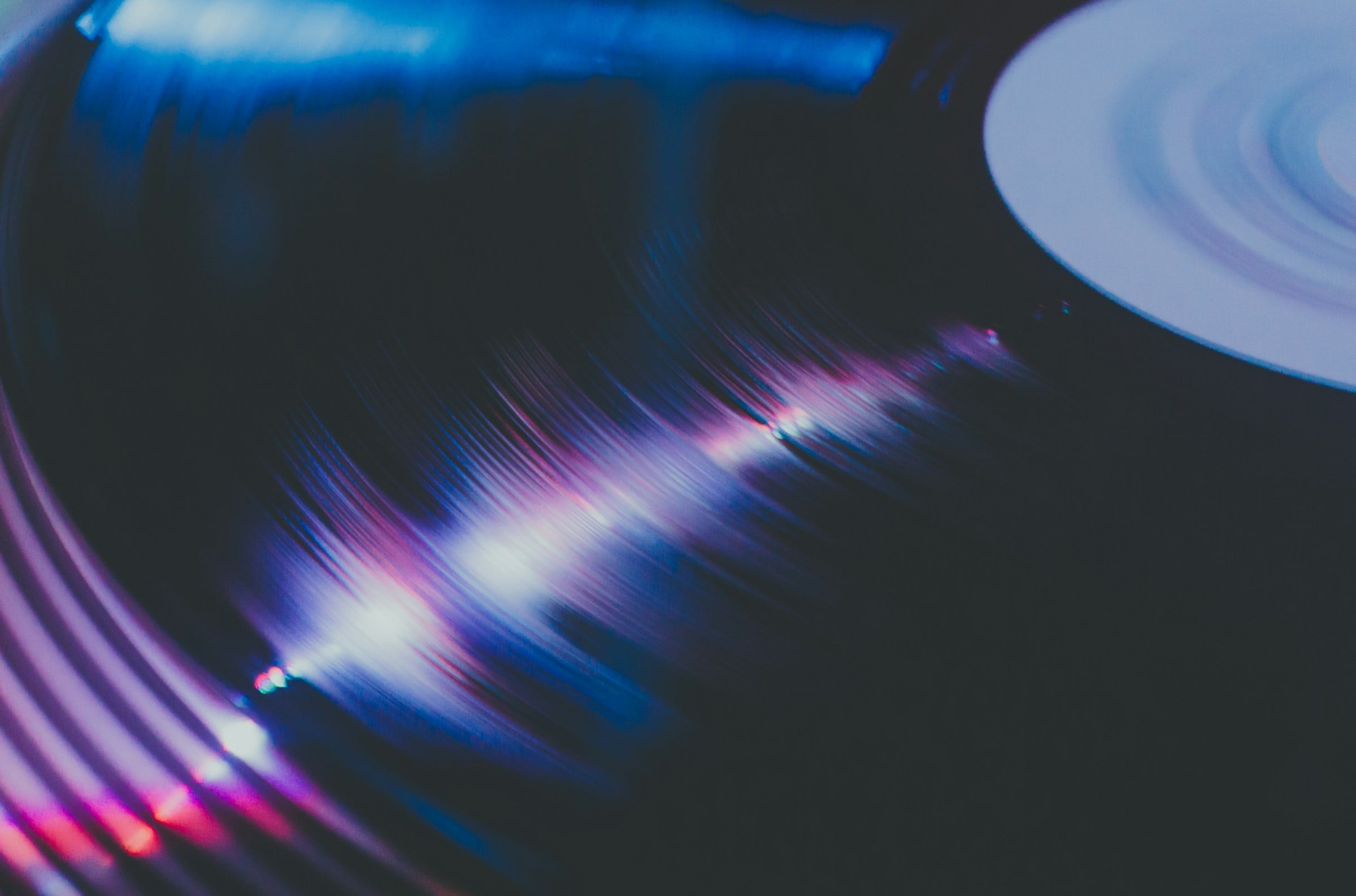 Close-up of a vinyl record with blue and magenta light streaks across the grooves